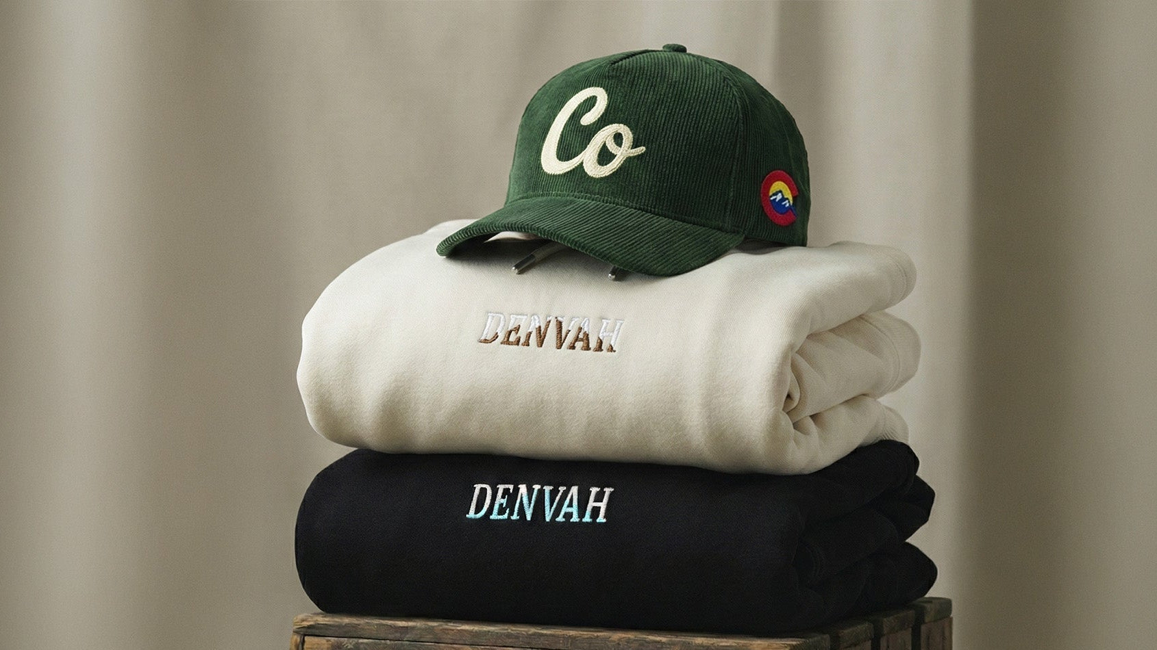 Stack of folded clothes with a green cap on a wooden block against a beige background