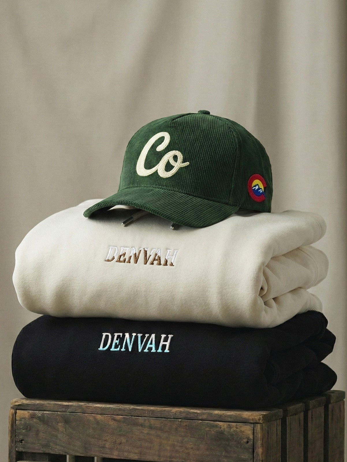 Stack of folded clothes with a green cap on a wooden crate against a beige background